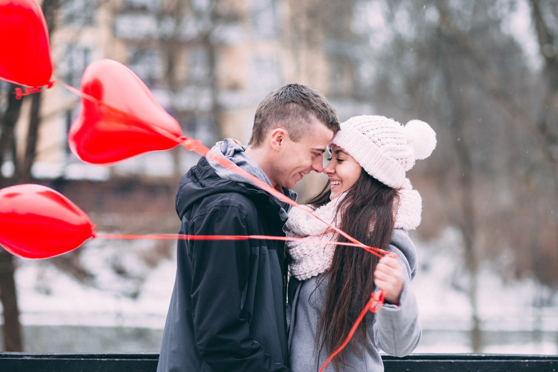 Ρομαντικό ζευγάρι αγκαλιασμένο, κρατάει κόκκινα μπαλόνια σε σχήμα καρδιάς