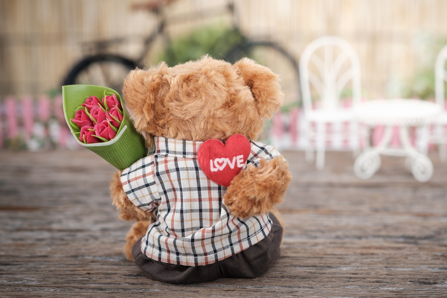 Ένα λούτρινο αρκουδάκι κρατά ένα μπουκέτο τριανταφυλλα και μία καρδιά σε ρουστίκ ξύλινο φόντο.