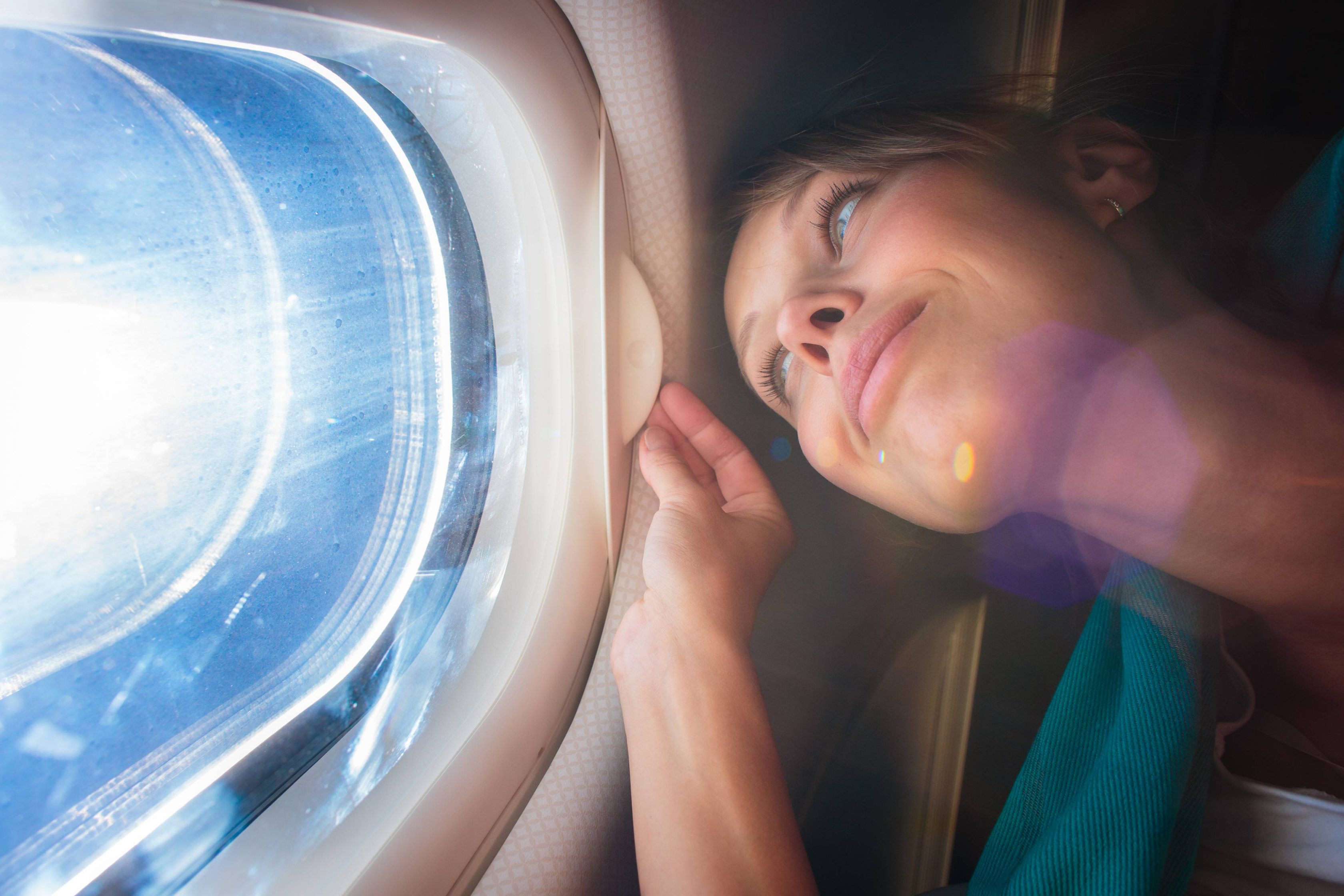 Μία νεαρή γυναίκα κοιτάζει τη θέα από το παράθυρο ενός αεροπλάνου.