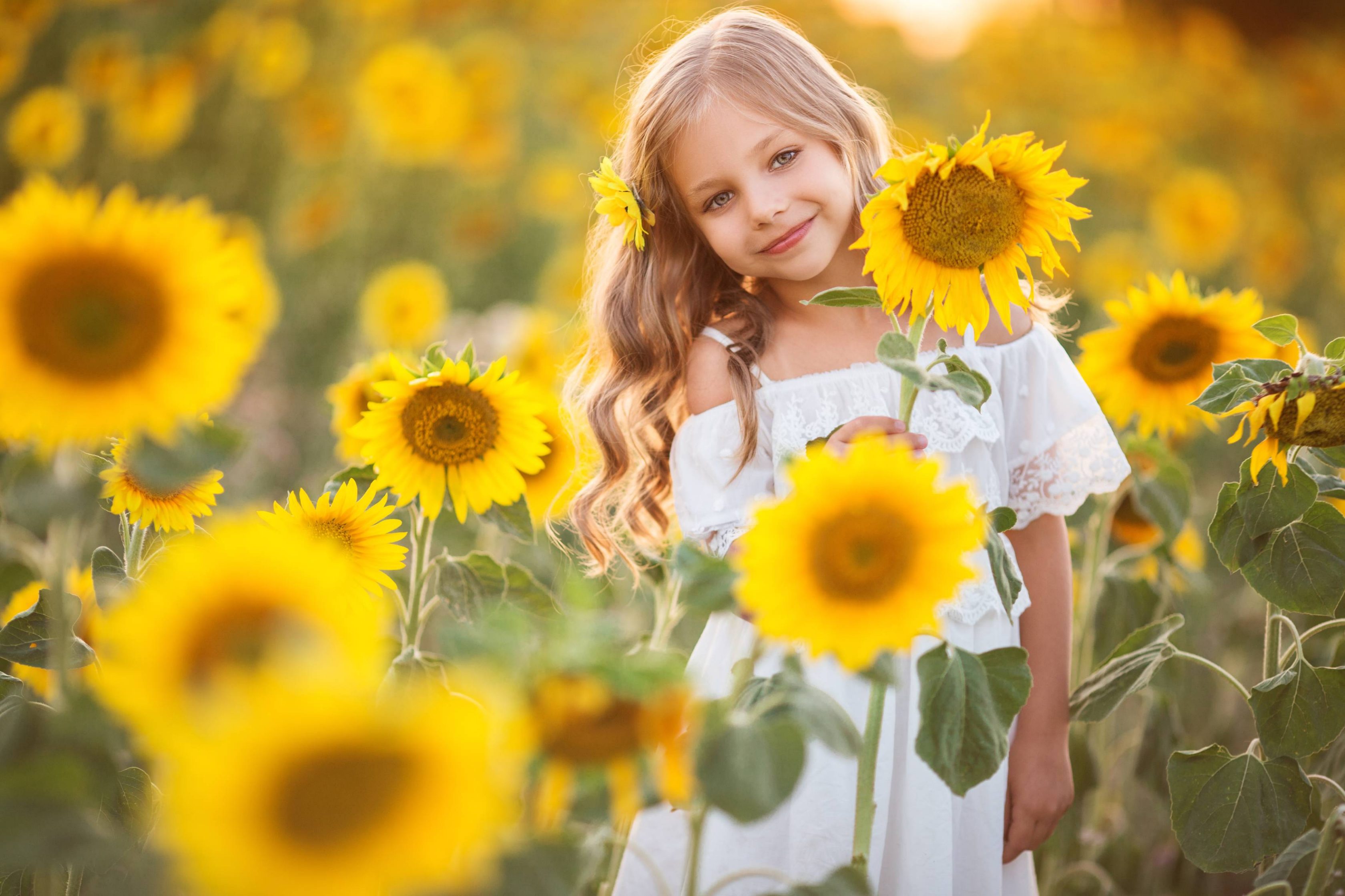 Μικρό κορίτσι χαμογελάει ανάμεσα σε κίτρινα λουλούδια.