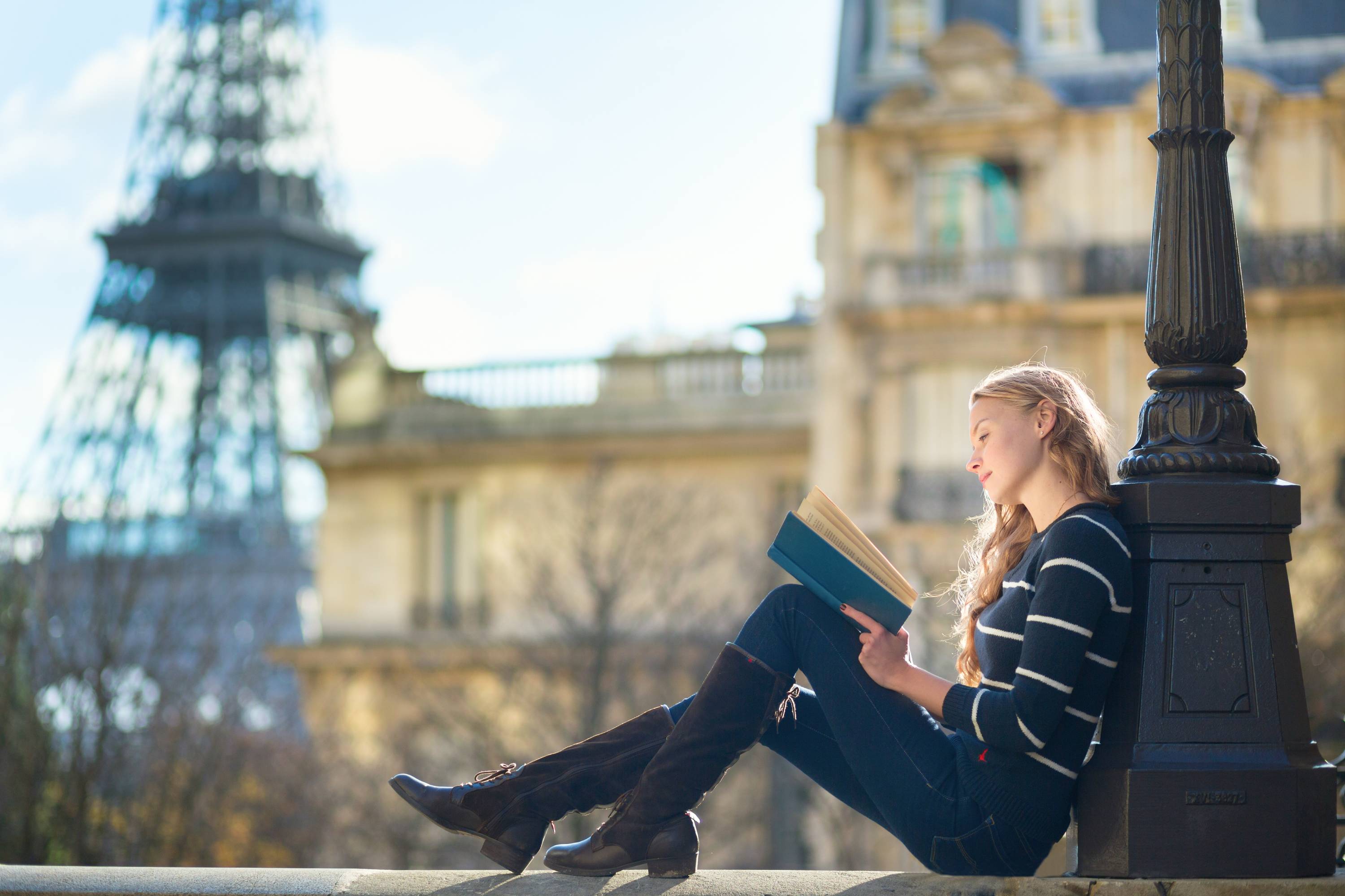 Νεαρή γυναίκα στο Παρίσι, διαβάζει βιβλίο με φόντο τον πύργο του Άιφελ