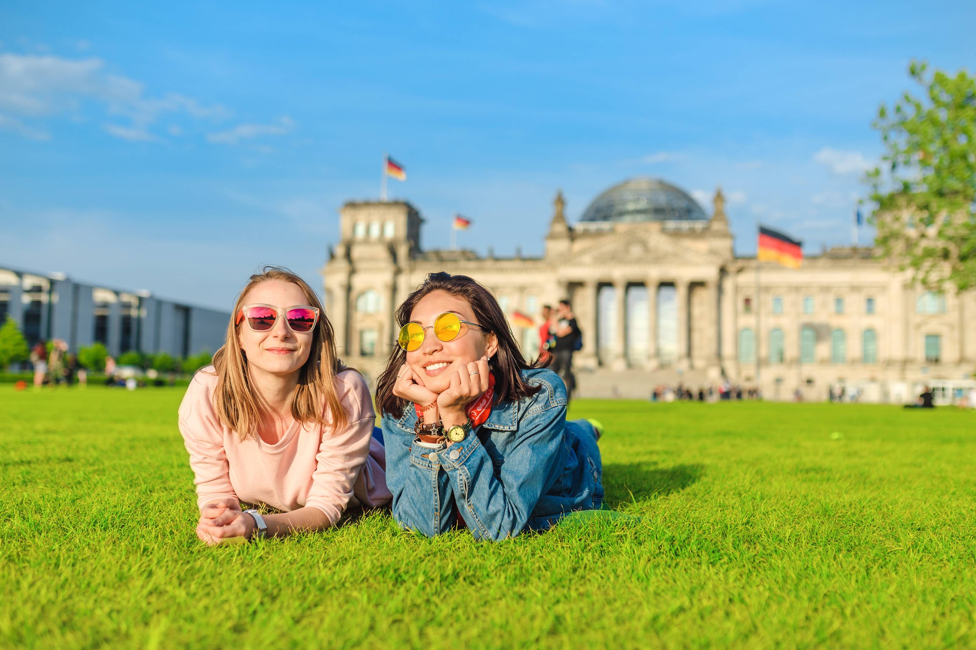 Δύο χαρούμενα κορίτσια ξαπλωμένα στο γρασίδι, φορώντας γυαλιά ηλίου, που σπουδάζουν στο Βερολίνο της Γερμανίας
