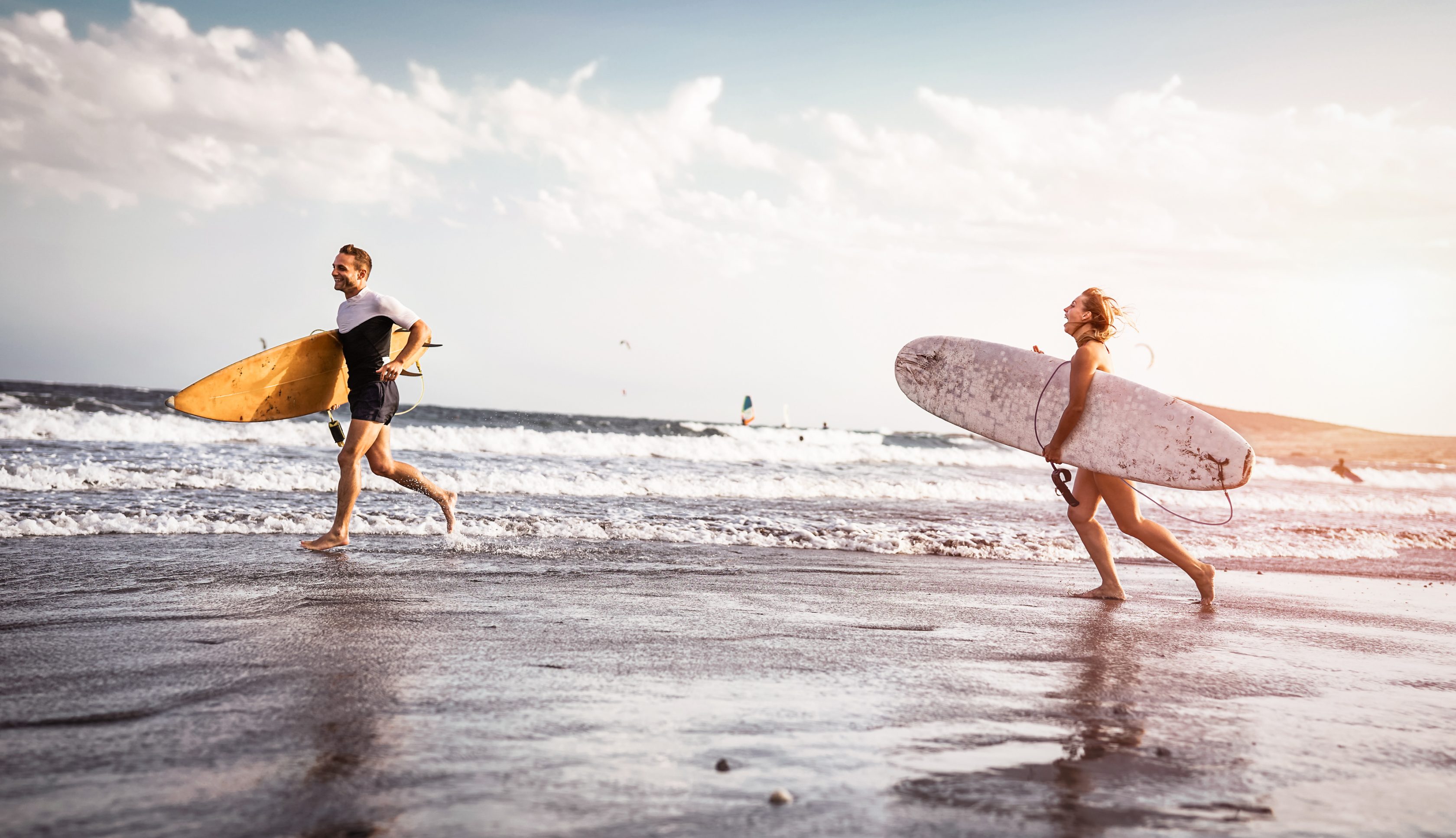 Ένα ζευγάρι από σέρφερ τρέχουν στην παραλία και διασκεδάζουν.